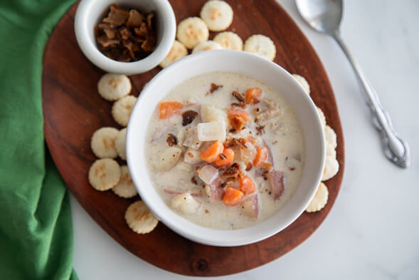 Bowl of New EnglandClamChowder on rown board with soda crackers