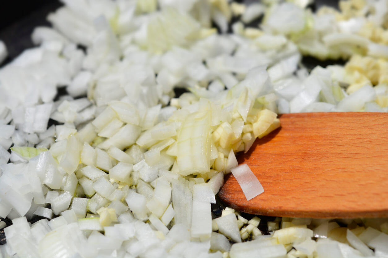 Detail of a pan with chopped onions and garlic in oil and a wooden spatula